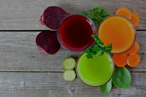 Top view of juice on a grey wood table alongside vegetables.