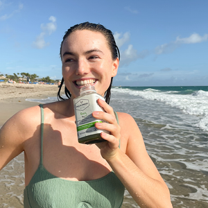 person holding envy cold pressed juice on tropical beach