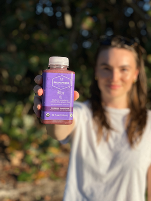 person holding purple bliss smoothie in focus on warm sunny day outside
