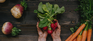 Dirt covered hands holding radishes surrounded by other fresh vegetables.
