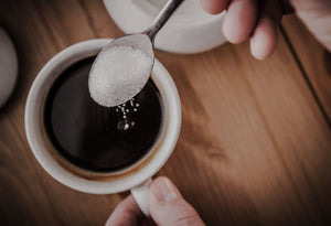 Sugar on a spoon being added to a coffee or tea.