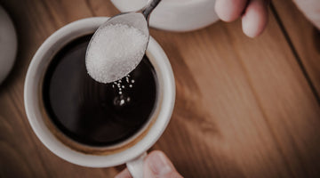 Sugar on a spoon being added to a coffee or tea.