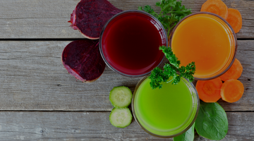 Top view of juice on a grey wood table alongside vegetables.