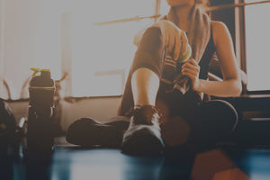 Woman in workout apparel sitting in a studio holding an apple. 