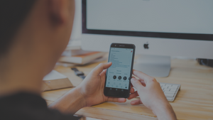 Man looking at phone while sitting at desktop computer.