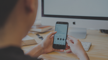 Man looking at phone while sitting at desktop computer.