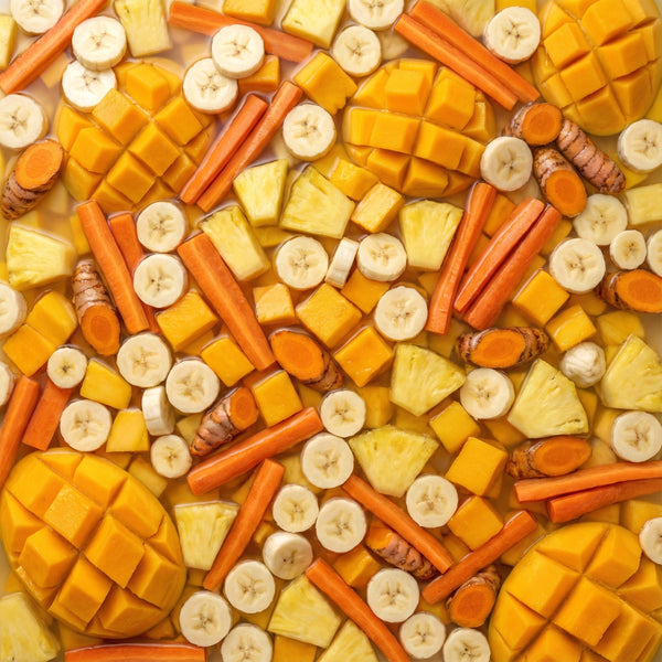 Assorted fruits including mangoes, carrots, and bananas and ginger pieces arranged in a pattern.