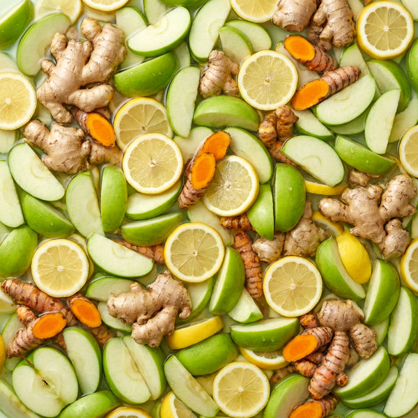 Mixture of sliced green apples, lemon slices, ginger pieces in a juice bath.