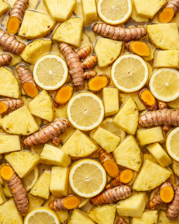 Mixture of pineapple chunks, lemon slices, turmeric roots floating on water.