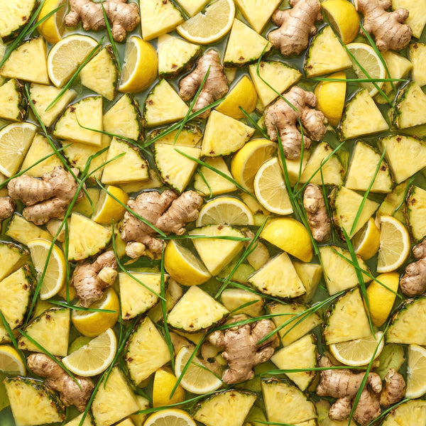 A close-up of sliced lemons, pineapples, and ginger in a water bath.