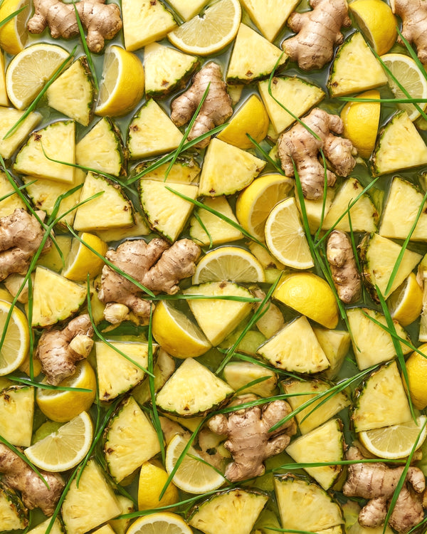 Floating fruit in a pan of juice with wheat grass, pineapple, lemons, and ginger.