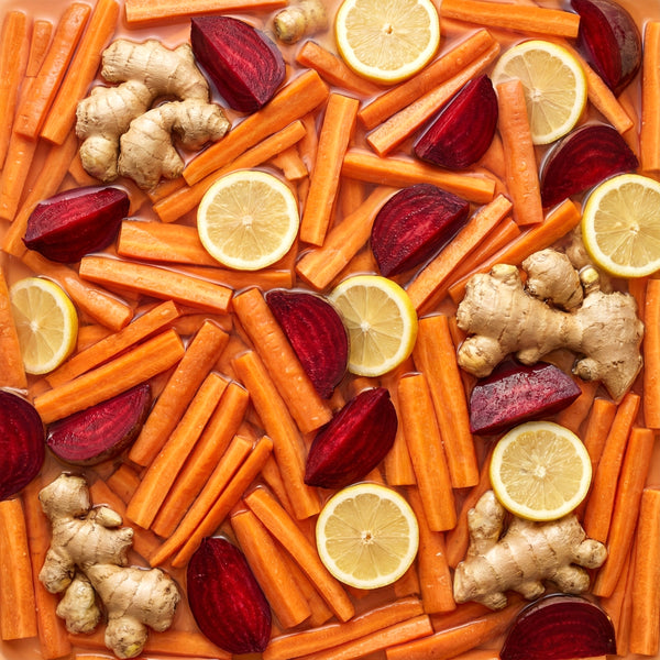 Assorted vegetables including carrots, beets, lemons, and ginger on a wooden surface.