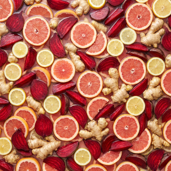 Colorful arrangement of sliced citrus fruits, beets, and ginger on a pink background
