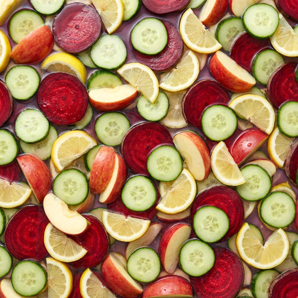 Colorful assortment of sliced fruits and vegetables including cucumbers, lemons, apples, and beets.