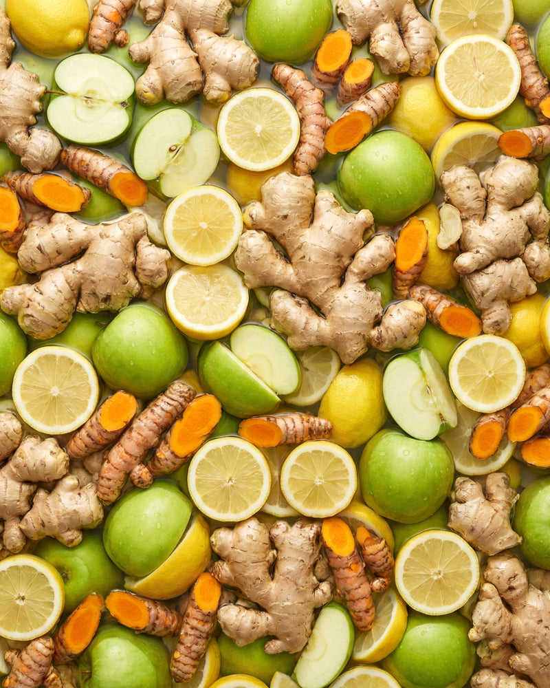 Assorted fruits, vegetables, and herbs including apples, lemons, ginger, and turmeric.