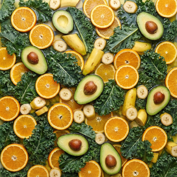 Pattern of oranges, avocados, bananas and kale arranged in a pattern.
