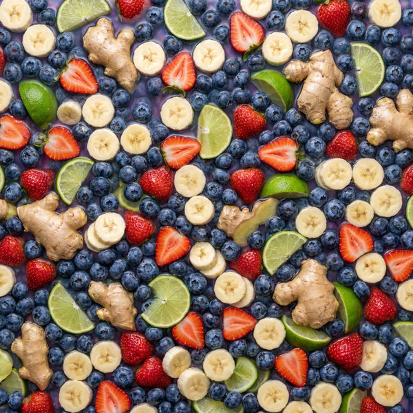 Assorted fruits including blueberries, strawberries, bananas, limes, and ginger on a colorful background.