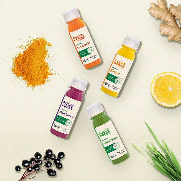 Four bottles of Pulp & Press juice on a light background with ingredients like turmeric, lemon, and cherries, ginger, lemon grass.