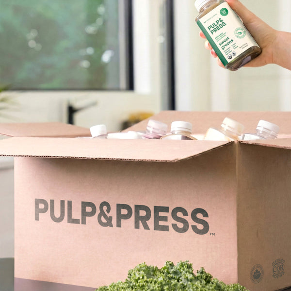 Person holding a bottle of 'Pulp&Press' product above a cardboard box with the brand name.