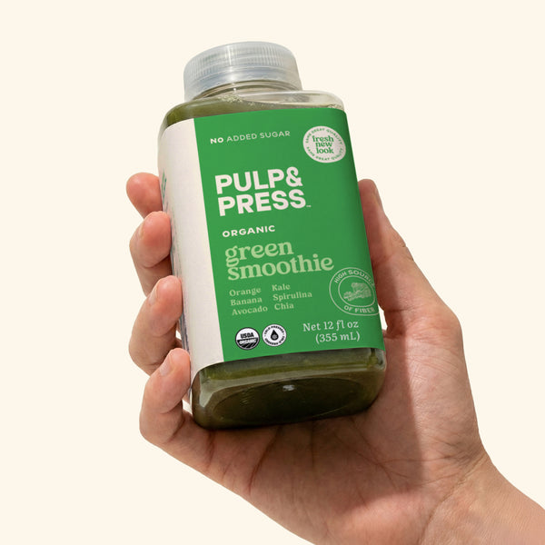 Hand holding a bottle of Pulp & Press green smoothie against a white background