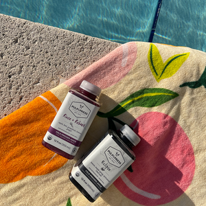 two bottles of cold pressed juice rinse & rebeet and eclipse on beach towel with swimming pool